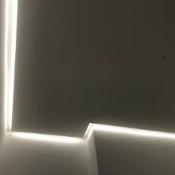 Nowoczesne oświetlenie sufitowe LED w narożniku pomieszczenia, tworzące minimalistyczny design z wyraźną linią światła.