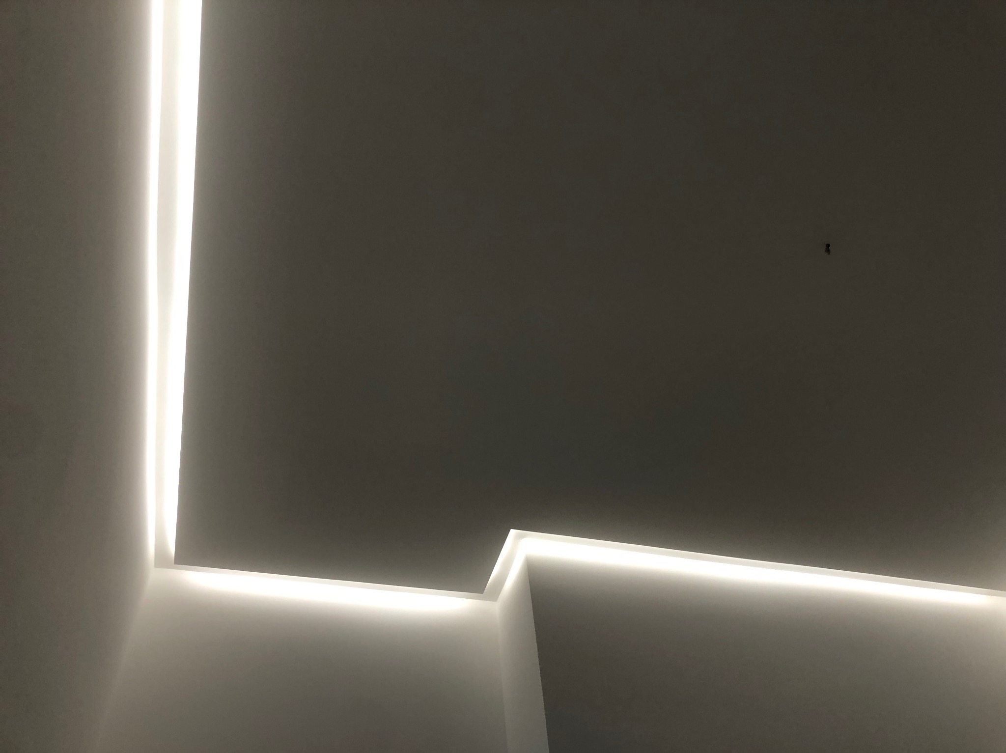 Nowoczesne oświetlenie sufitowe LED w narożniku pomieszczenia, tworzące minimalistyczny design z wyraźną linią światła.