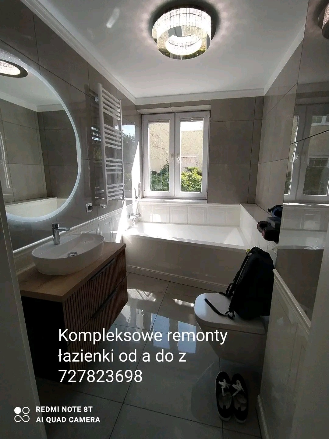 Wyremontowana łazienka z owalnym lustrem, umywalką nablatową na szafce z lamelami, grzejnikiem drabinkowym, wanną, oświetleniem sufitowym i błyszczącymi płytkami podłogowymi.