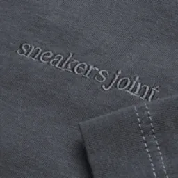 Szara koszulka z wyhaftowanym napisem 'sneakersjoint' w dolnym rogu, widoczne szwy na rękawie.
