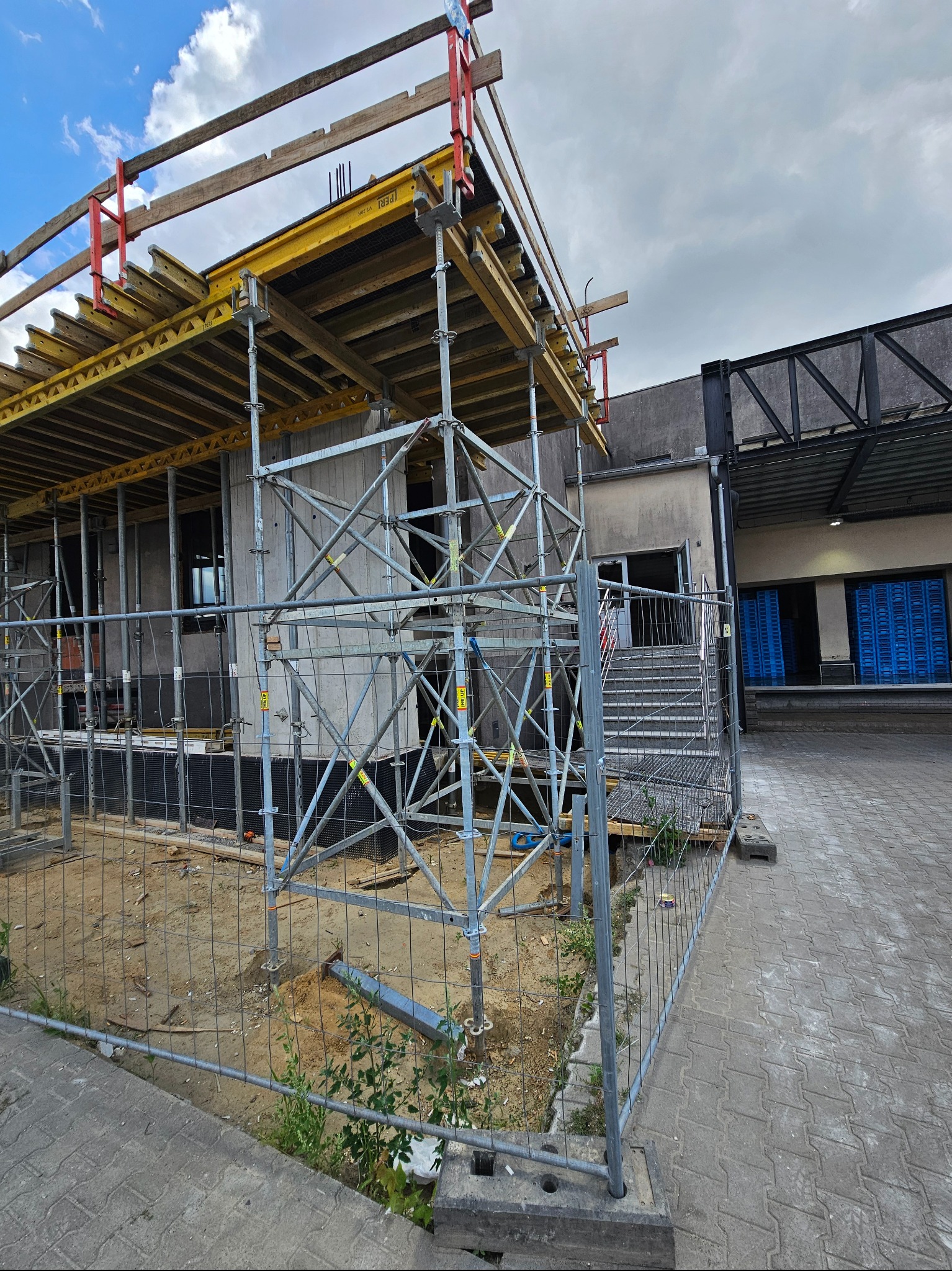 Budowa obiektu z szalunkiem i rusztowaniem, widok z zewnątrz, ogrodzenie tymczasowe. Elementy konstrukcyjne w trakcie wznoszenia, widoczne detale szalunku.