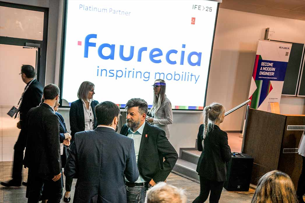 Uczestnicy konferencji w kuluarach rozmawiają, na ekranie wyświetlony logotyp firmy Faurecia, w tle widoczny baner z hasłem 'Become a modern engineer'.