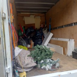 Piotr Jaśkowiak Złota Rączka - Wnętrze furgonetki załadowane workami, meblami i choinką, gotowe do transportu. Widoczne zabezpieczenia ładunku i tablica rejestracyjna pojazdu.