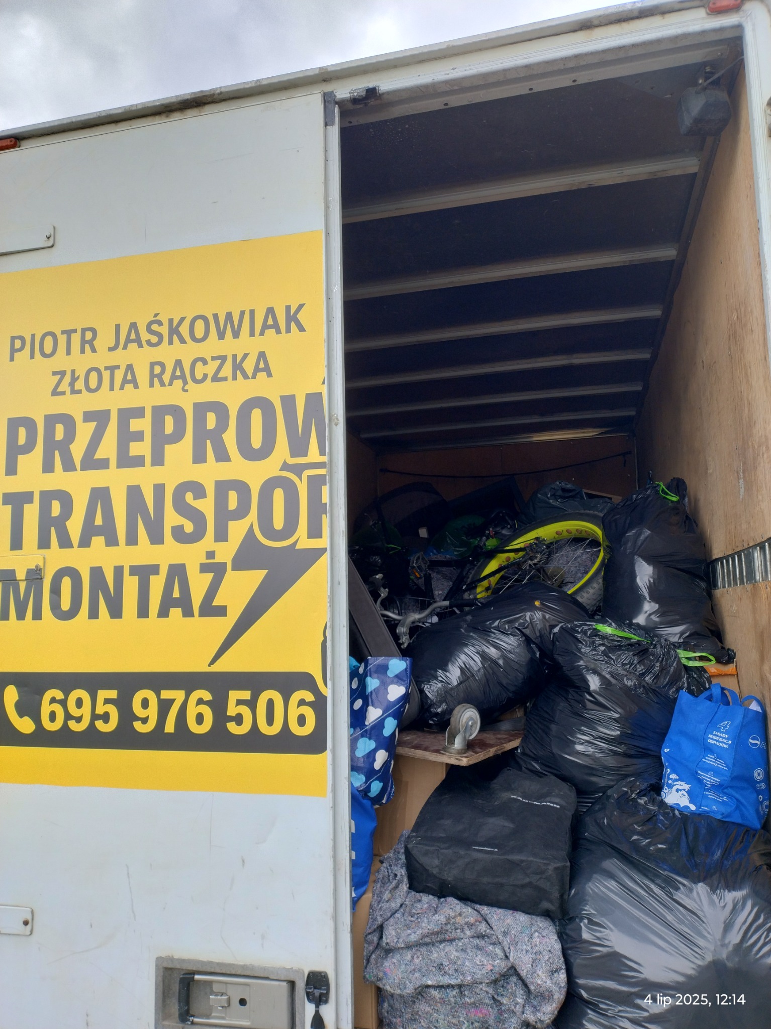 Wnętrze busa transportowego wypełnione workami i rowerem, widoczny numer telefonu firmy Piotr Jaśkowiak Złota Rączka oferującej przeprowadzki, transport i montaż.