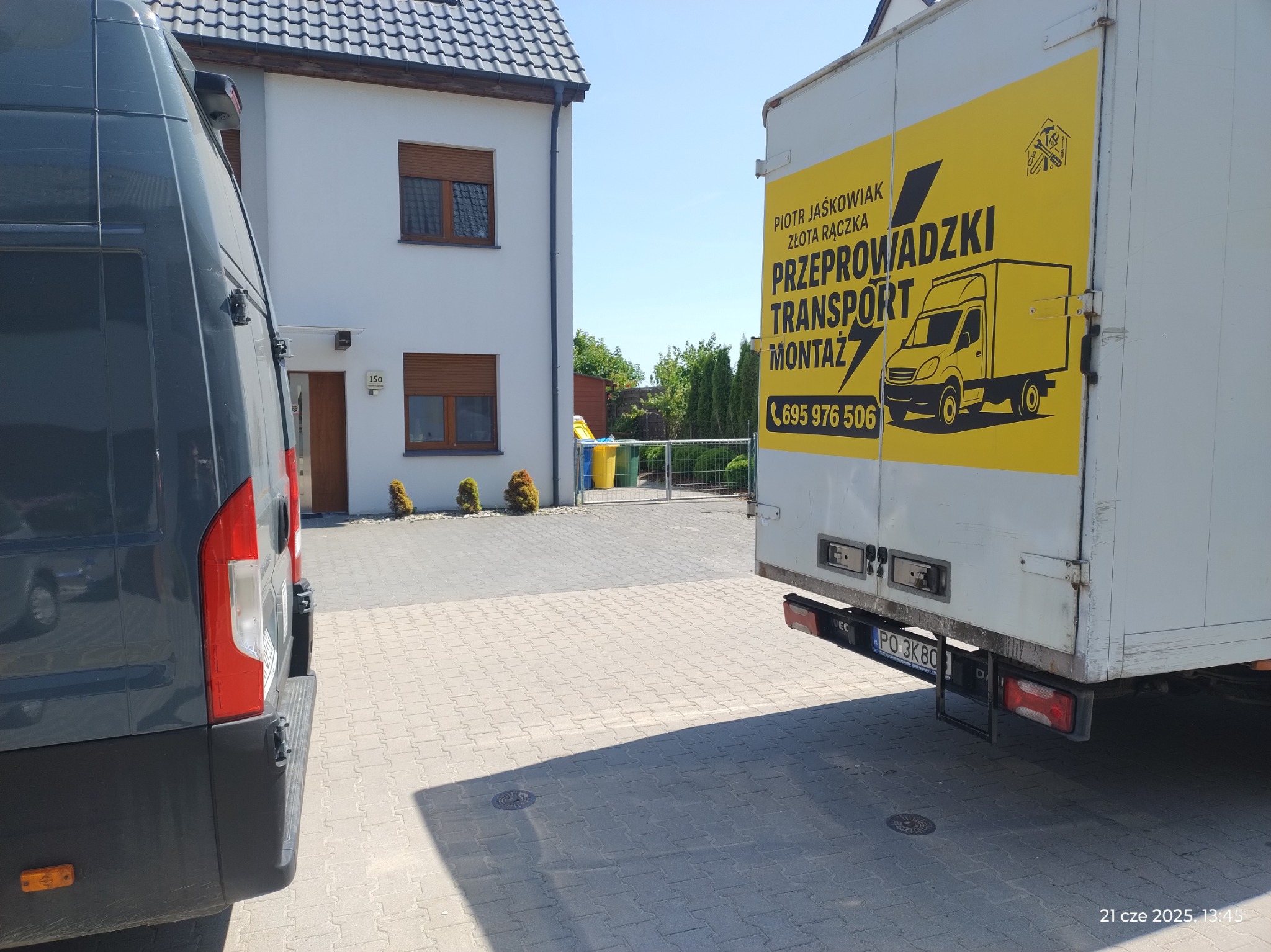 Dwa busy na posesji przed domem. Na jednym z nich żółta reklama firmy transportowej z numerem telefonu i napisem: Przeprowadzki, Transport, Montaż.