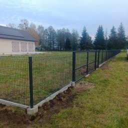 Sebastian Drejka - Nowoczesne ogrodzenie panelowe z podmurówką betonową, widoczne na tle zielonego trawnika i drzew. Słupki w kolorze grafitowym. Widok z perspektywy ziemi.