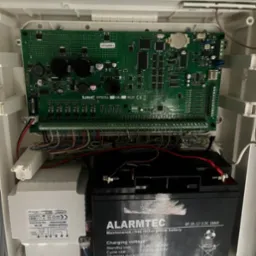 Centrala alarmowa Satel Integra 128 Plus w obudowie, z widoczną płytą główną, transformatorem Pulsar i akumulatorem Alarmtec, połączona przewodami.