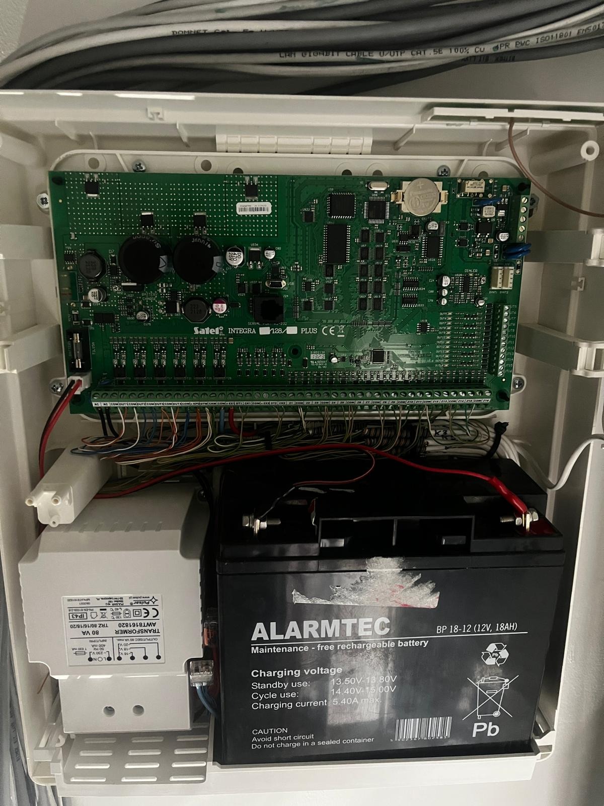 Centrala alarmowa Satel Integra 128 Plus w obudowie, z widoczną płytą główną, transformatorem Pulsar i akumulatorem Alarmtec, połączona przewodami.