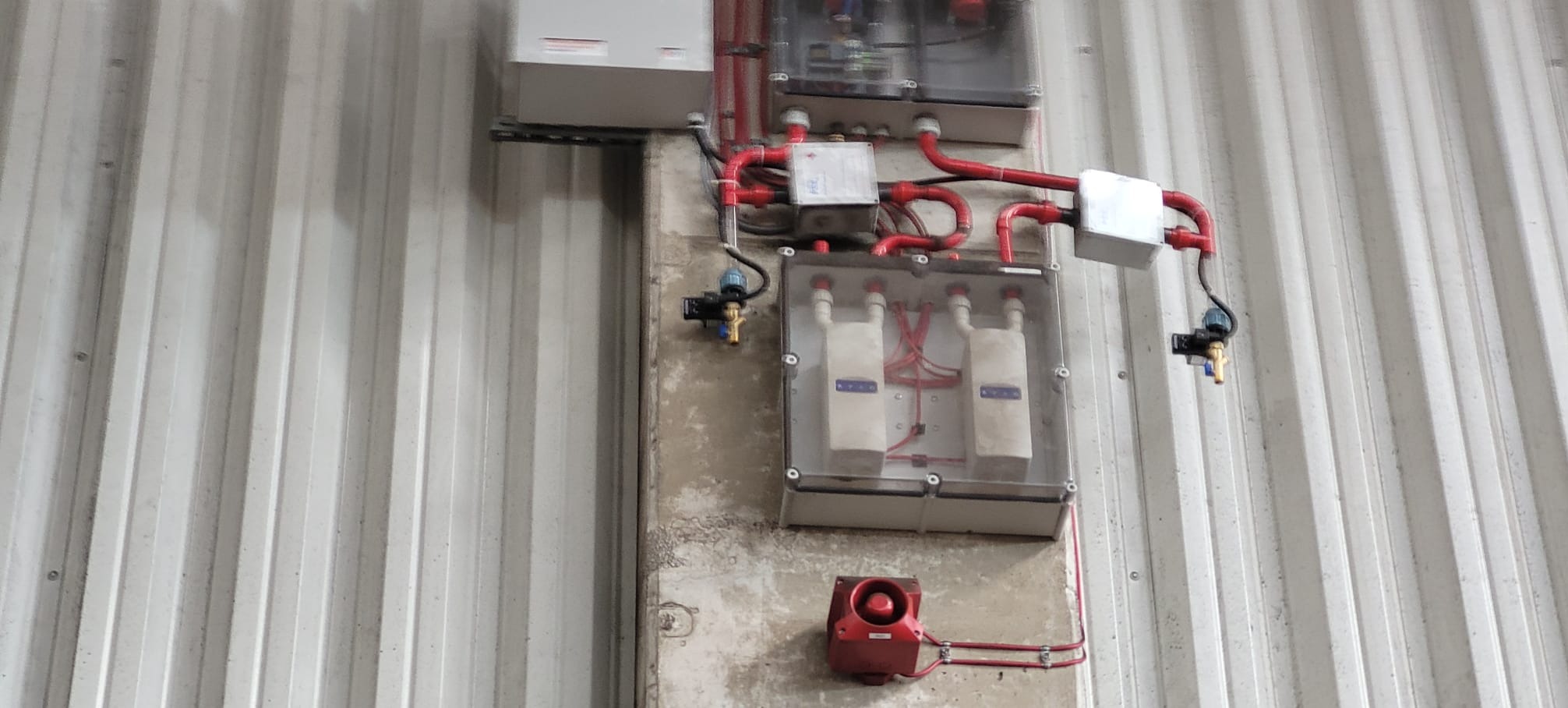 Instalacja alarmowa z czujnikami i przewodami w obudowach ochronnych, zamontowana na ścianie w Brzozie. System sygnalizacji pożaru.