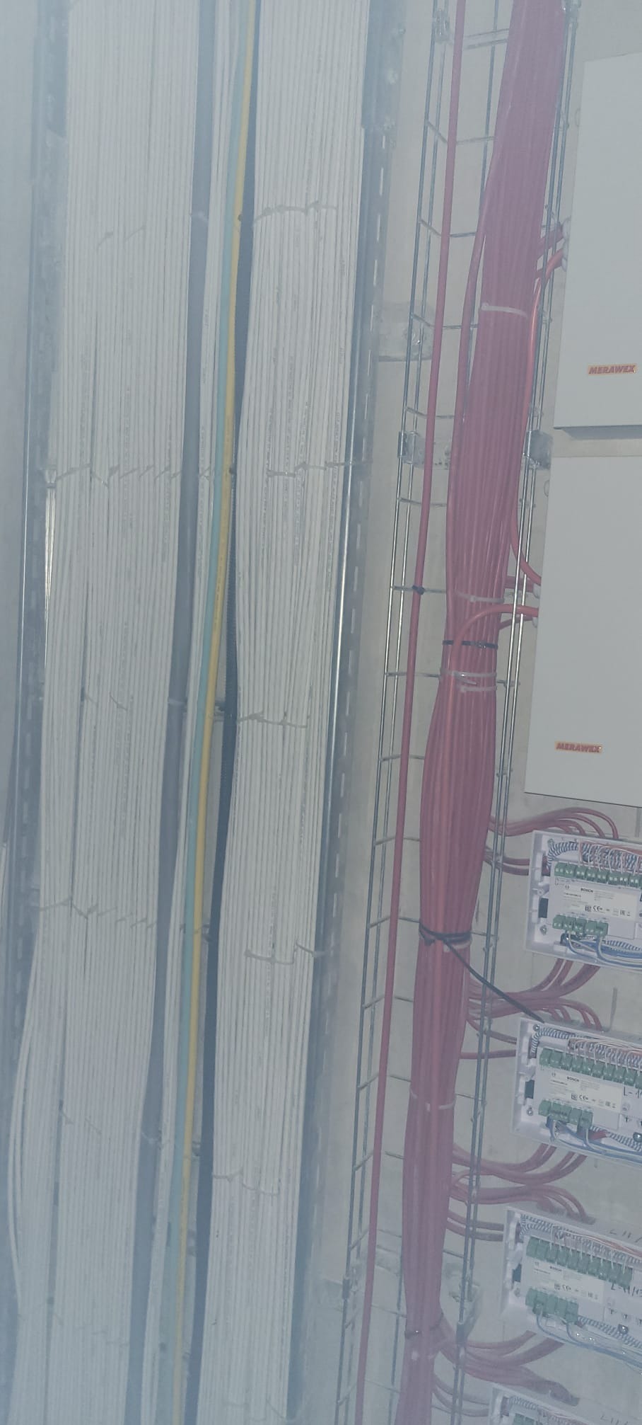 Kable elektryczne w korytkach, białe i czerwone, z widocznymi panelami sterowania. Układ kabli w budynku, instalacja elektryczna w trakcie montażu.