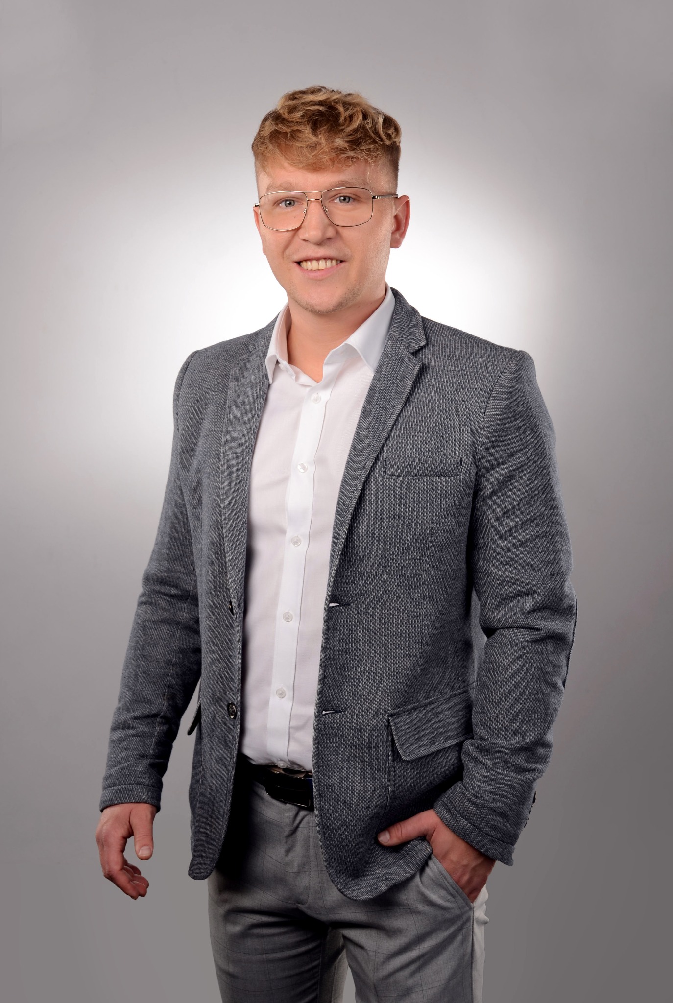 Uśmiechnięty mężczyzna w okularach i szarej marynarce na jasnym tle. Portret agenta nieruchomości w eleganckim stroju.