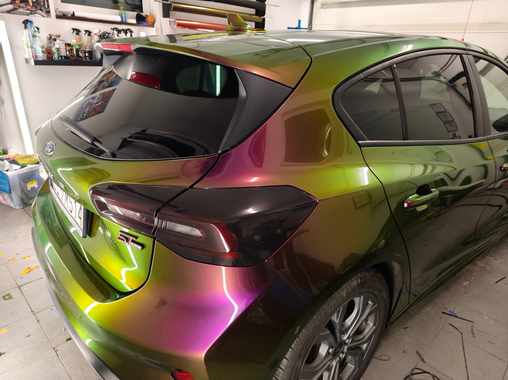 Oklejony folią chameleon Ford Focus ST-Line, widok z tyłu. Folia zmienia kolor od zieleni do fioletu w zależności od kąta padania światła. Widoczne detale: felgi, lampy.