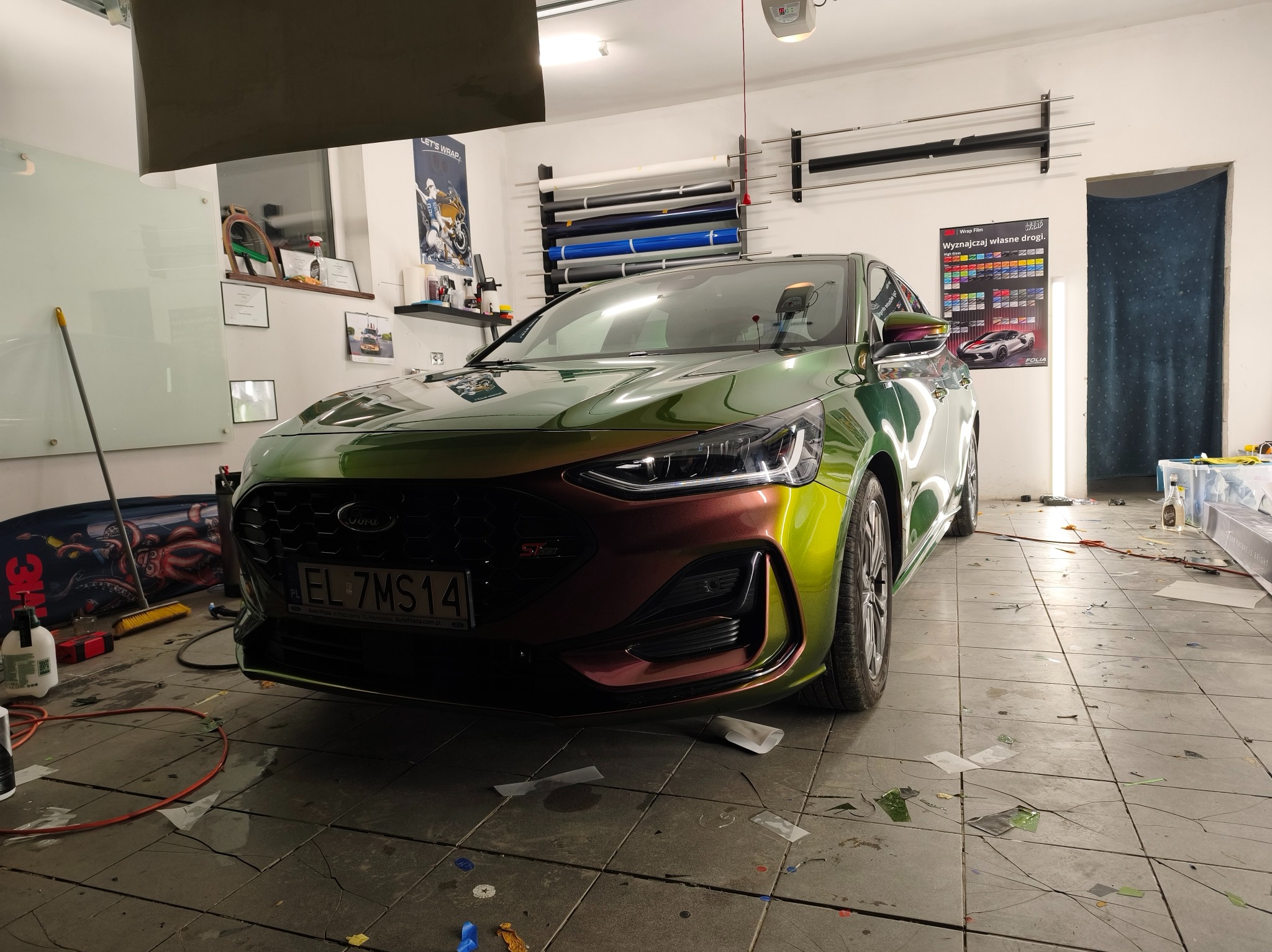 Ford Focus po oklejeniu folią zmieniającą kolor, widoczny w warsztacie z rolkami folii i narzędziami. Efektowna metamorfoza karoserii.