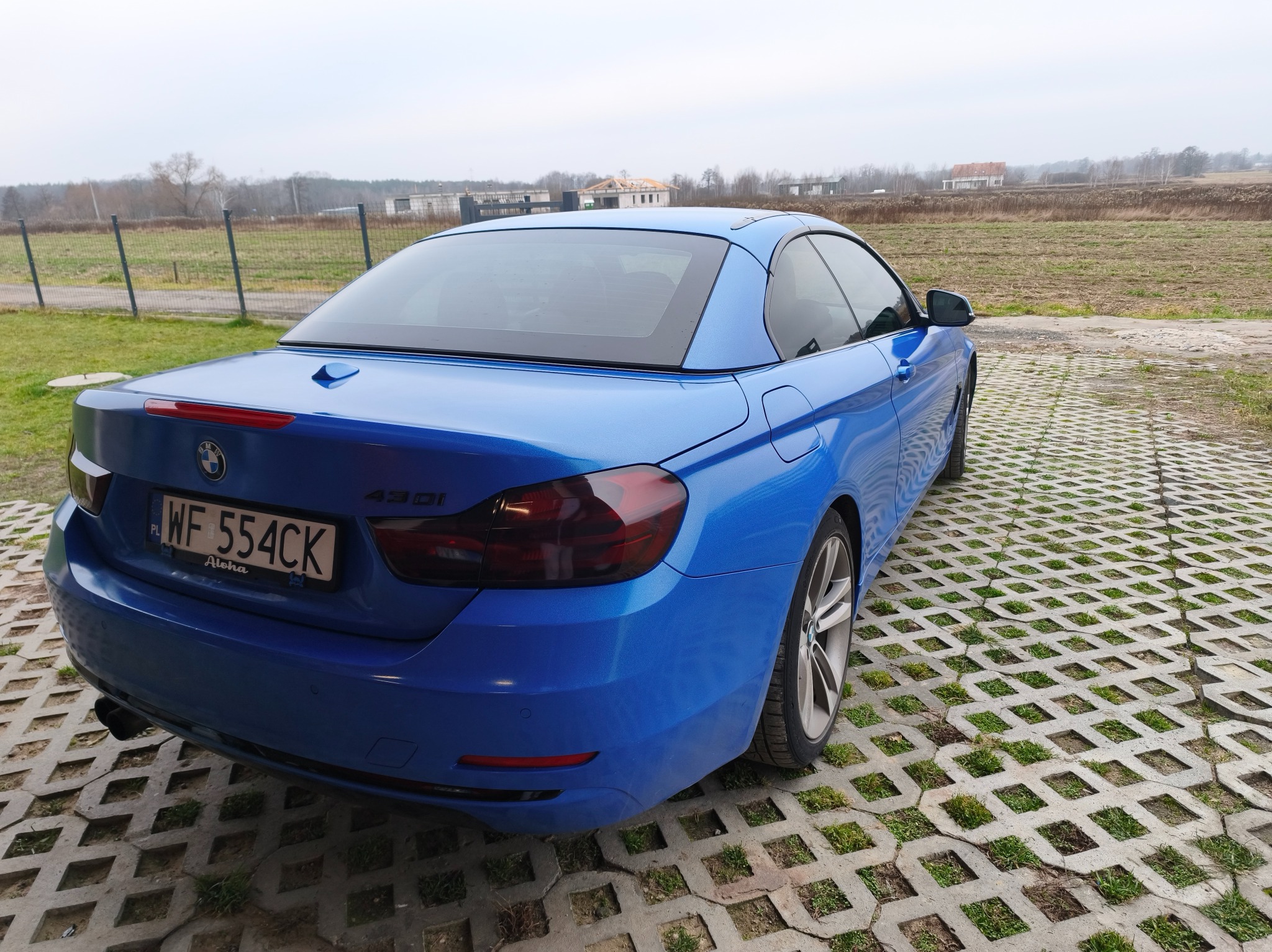 Błękitny kabriolet BMW 430i z przyciemnionymi lampami, zaparkowany na ażurowej kostce. Widok z tyłu, tablica rejestracyjna WF 554CK.