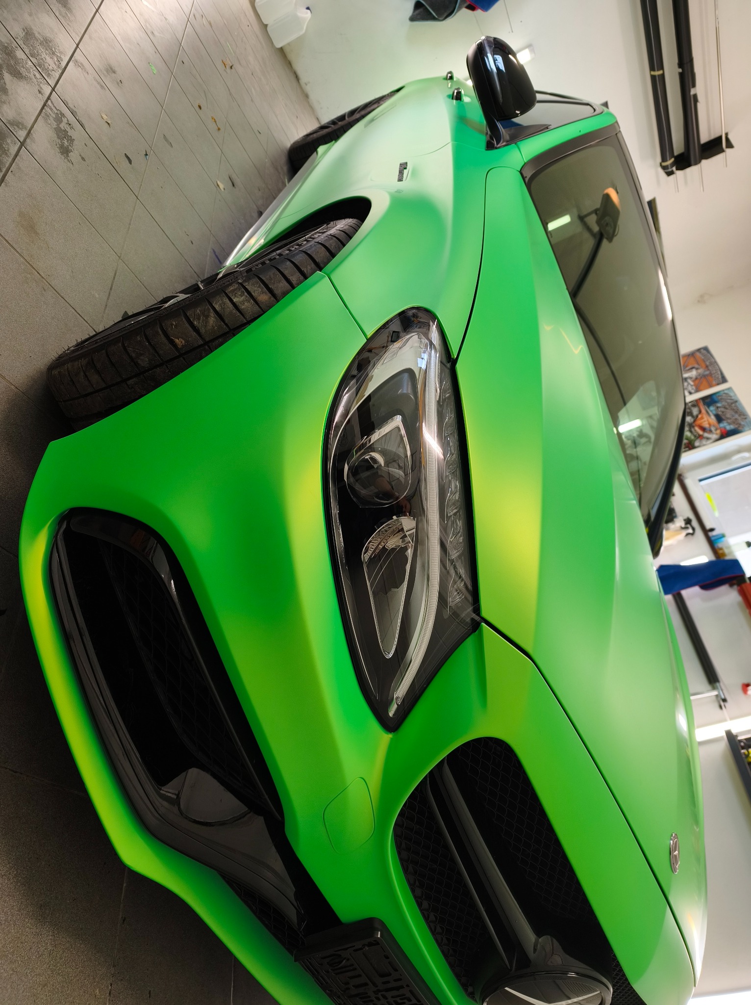 Jaskrawo zielony samochód po oklejeniu folią, widoczny z bliska, z detalami reflektora i grilla. Matowe wykończenie folii podkreśla kształty karoserii.