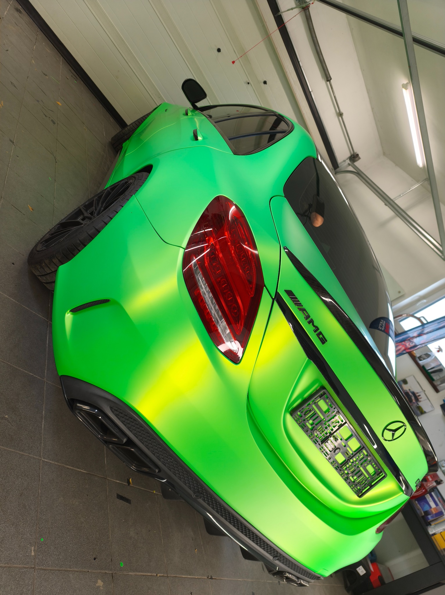 Jaskrawozielony, matowy Mercedes-AMG po oklejeniu folią, widoczny z tyłu w warsztacie. Charakterystyczne logo AMG i czarne detale podkreślają sportowy wygląd.