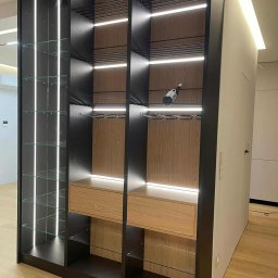 Unikalna Forma Piotr Sulik - Nowoczesna szafa wnękowa z oświetleniem LED i szklanymi półkami, wykonana na wymiar we Wrocławiu. Czarny korpus, drewniane elementy, minimalistyczny design.