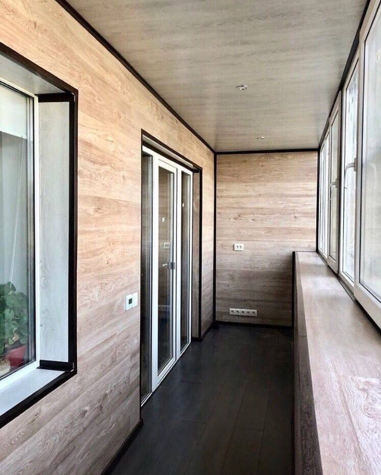 Wnętrze balkonu wykończonego panelami ściennymi imitującymi drewno, z czarną podłogą i białymi ramami okiennymi oraz drzwiami balkonowymi.