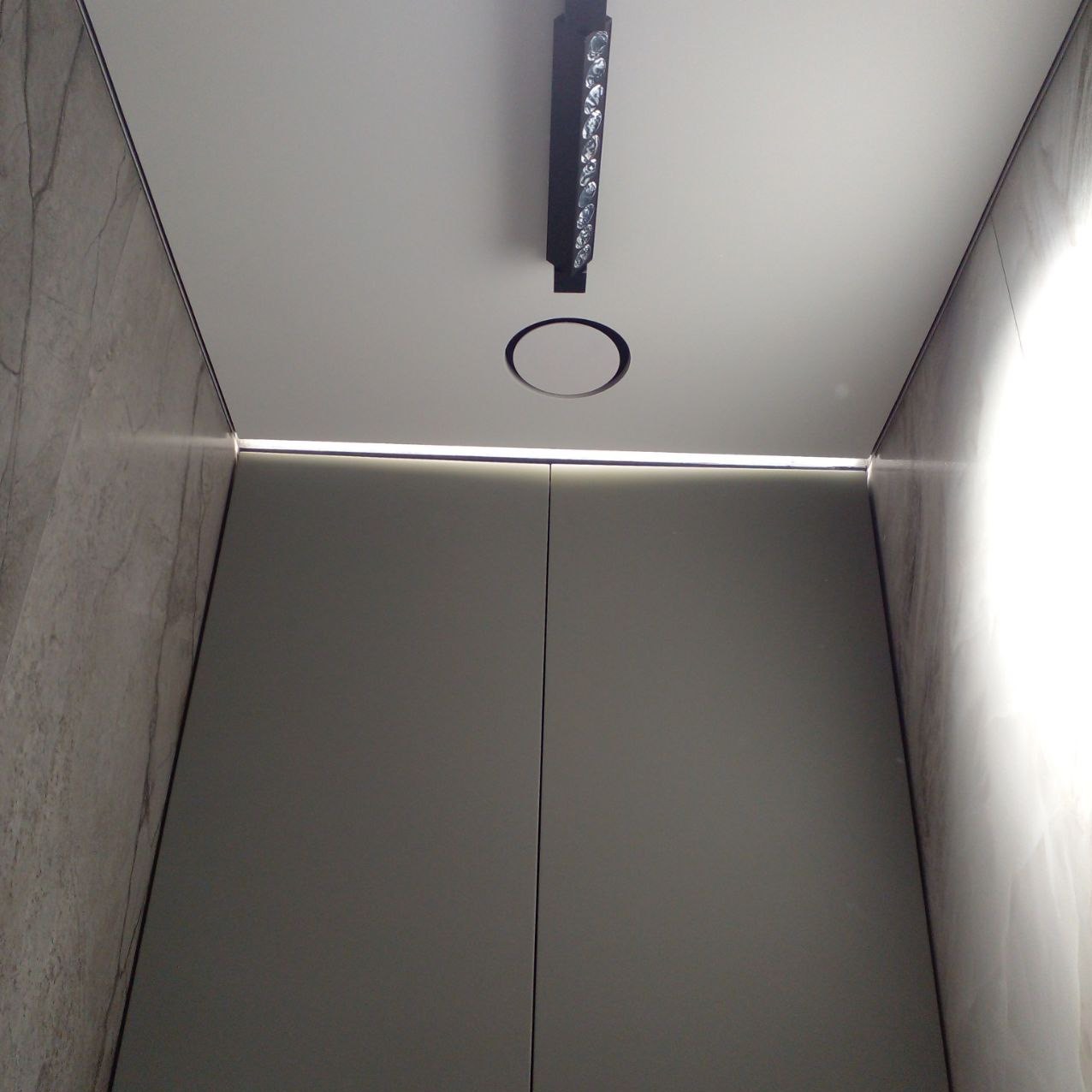 Nowoczesna łazienka z szarymi płytkami imitującymi marmur, gładkimi szarymi frontami szafek, oświetleniem LED liniowym i punktowym w suficie.