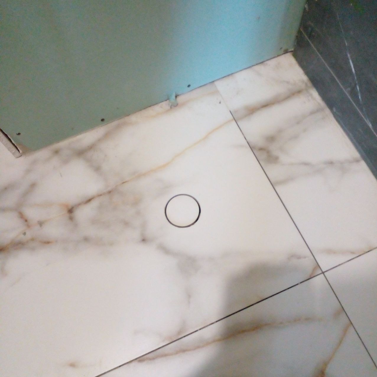 Podłoga z białych płytek imitujących marmur, z odpływem liniowym w trakcie montażu, widoczna płyta karton gips na ścianie.