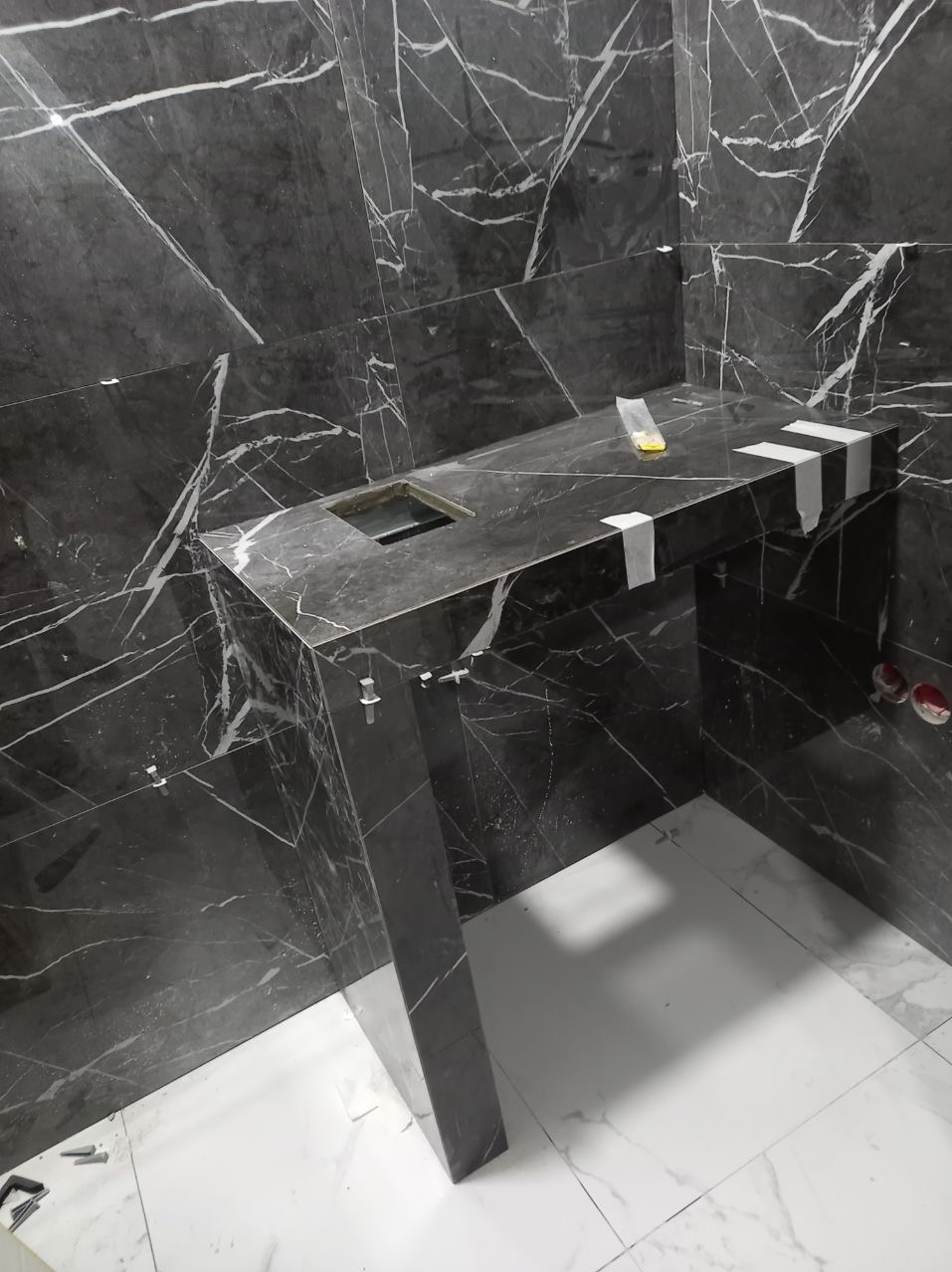 Montaż umywalki z czarnego marmuru z białymi żyłami w łazience, widoczne białe plamy po kleju i przyssawki do płytek.