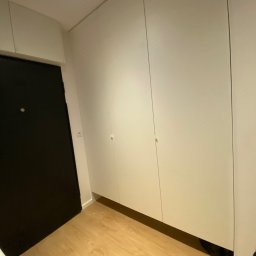 Kacper Stanisławski - Biała szafa wnękowa z minimalistycznymi uchwytami, dopasowana do przestrzeni przy drzwiach, Środa Wielkopolska. Jasne drewno podłogi.