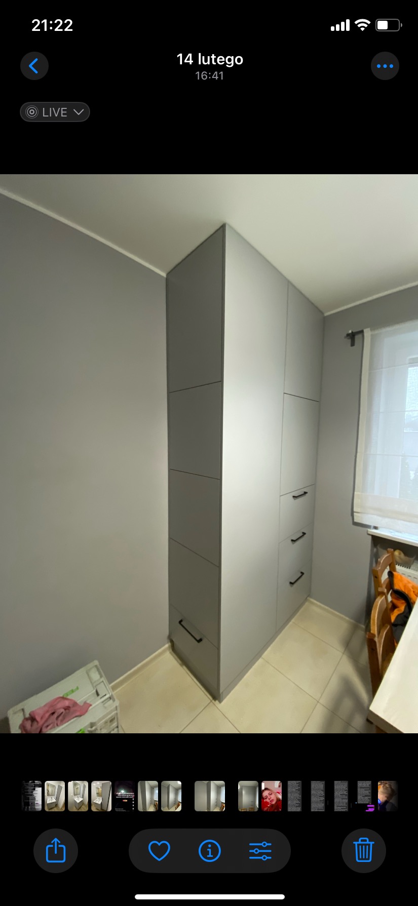 Szara szafa wnękowa z trzema szufladami i górną częścią z drzwiami, dopasowana do koloru ścian, z czarnymi uchwytami, stojąca na jasnych płytkach, widok z boku.