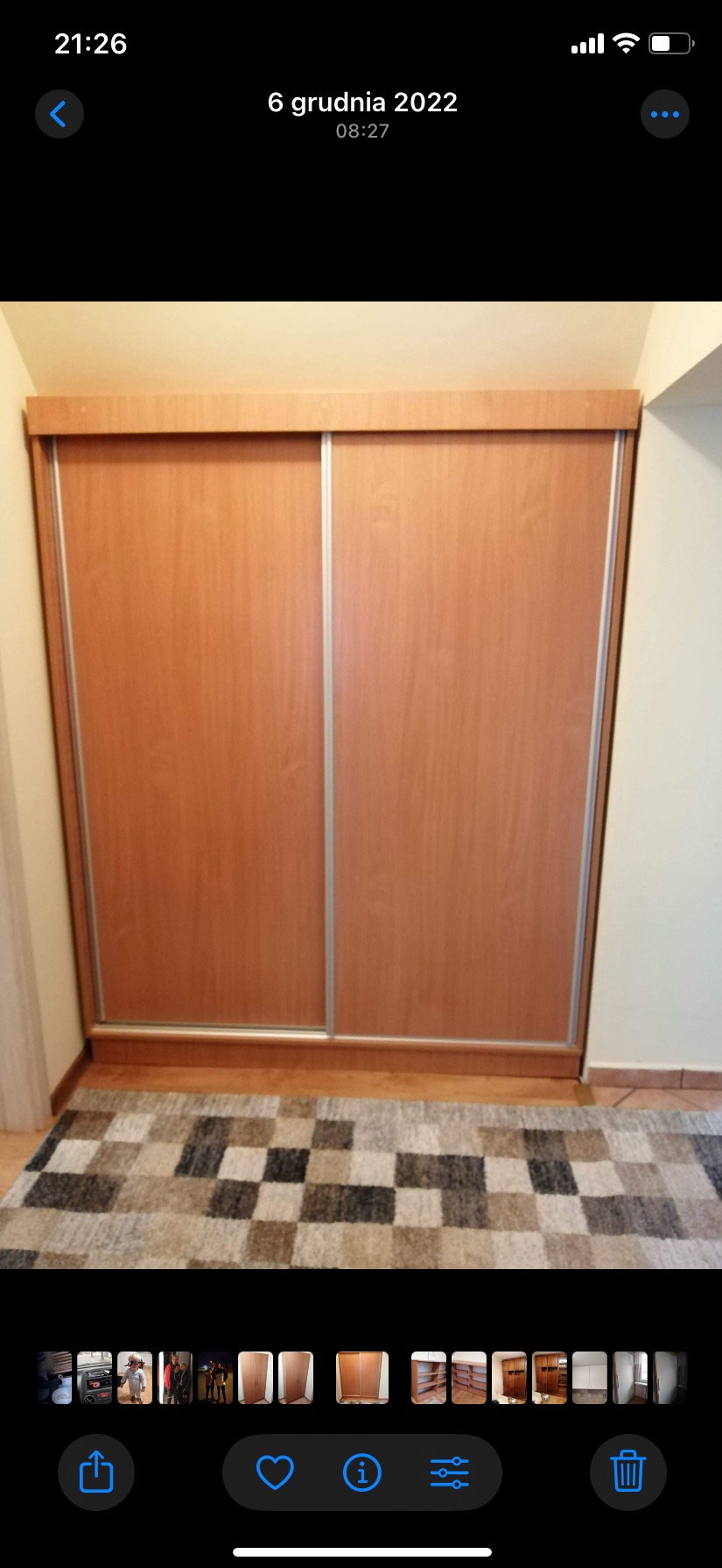 Zamknięta szafa wnękowa z przesuwnymi drzwiami o jasnym, drewnopodobnym wykończeniu i srebrnych listwach, na tle beżowej ściany i dywanu w szaro-brązową szachownicę.