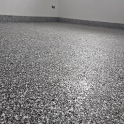 Patryk Borysiuk Matrix Floor - Szara, drobnoziarnista posadzka w jasnym pomieszczeniu, widoczne łączenie ze ścianą.