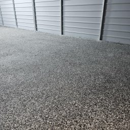 Patryk Borysiuk Matrix Floor - Szara, drobnoziarnista posadzka w hali przemysłowej z blachy trapezowej, widok z niskiej perspektywy.