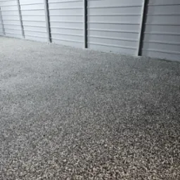 Szara, drobnoziarnista posadzka w hali przemysłowej z blachy trapezowej, widok z niskiej perspektywy.