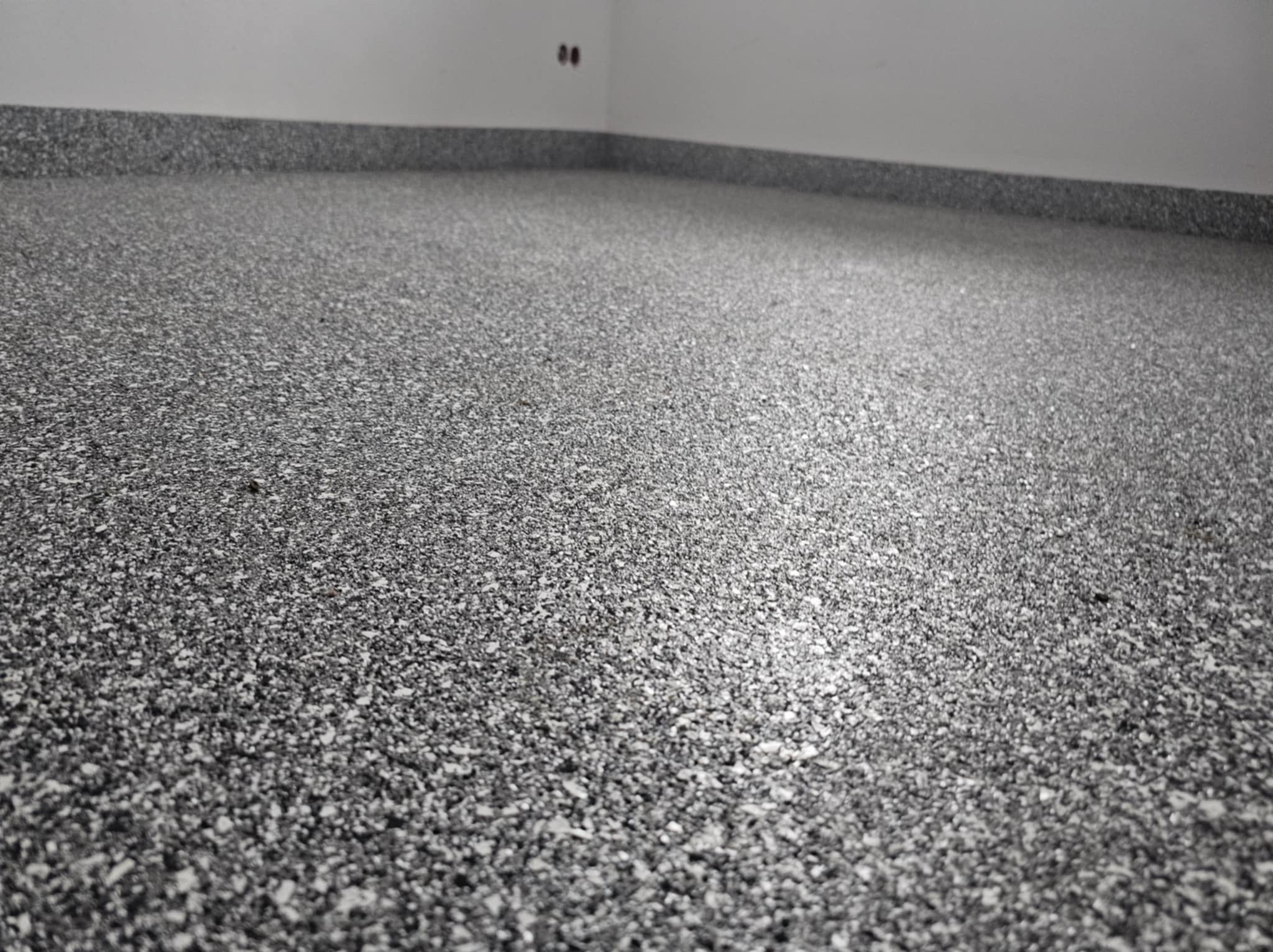 Szara, drobnoziarnista posadzka w jasnym pomieszczeniu, widoczne łączenie ze ścianą.