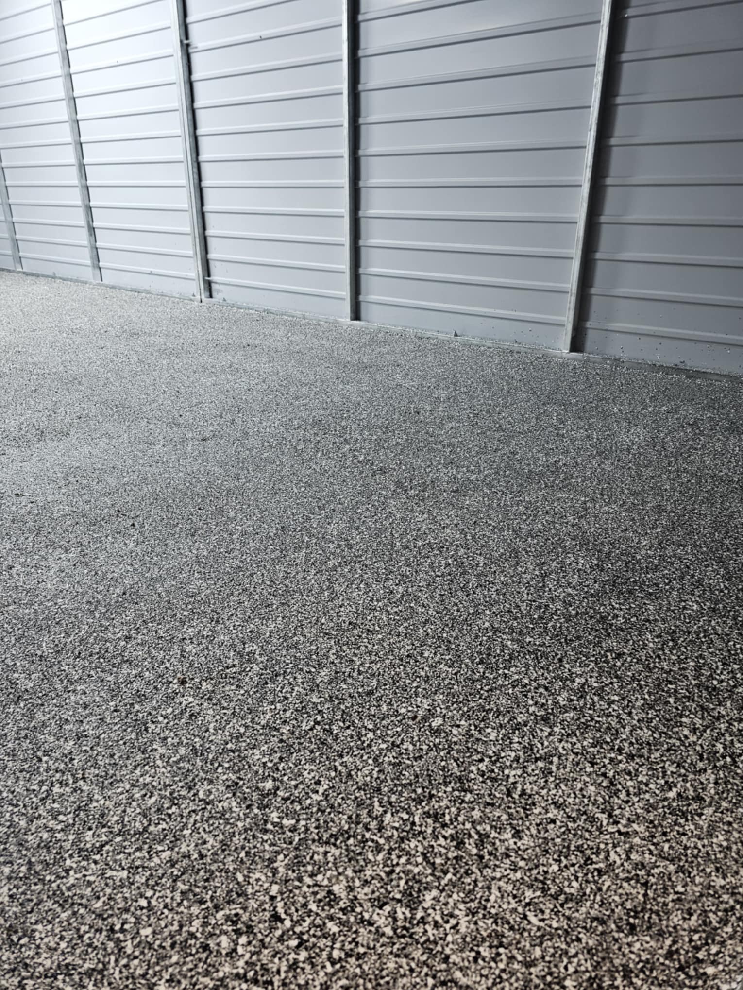 Szara, drobnoziarnista posadzka w hali przemysłowej z blachy trapezowej, widok z niskiej perspektywy.