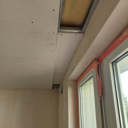 HORIZON VITALII VDOVYCHENKO - Montaż sufitu podwieszanego z płyt kartonowo-gipsowych, widoczne profile metalowe i izolacja. Okno zabezpieczone folią malarską. Etap prac wykończeniowych.