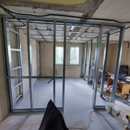 HORIZON VITALII VDOVYCHENKO - Stelaż z profili metalowych, przygotowany do montażu płyt gipsowo-kartonowych. Widoczne profile sufitowe i ścienne, okno w tle. Wnętrze w trakcie prac wykończeniowych.