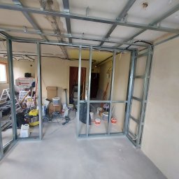 HORIZON VITALII VDOVYCHENKO - Metalowa konstrukcja ścian działowych w trakcie montażu, widoczne profile sufitowe, przewody elektryczne, narzędzia i materiały budowlane w tle. Świeża wylewka podłogowa.