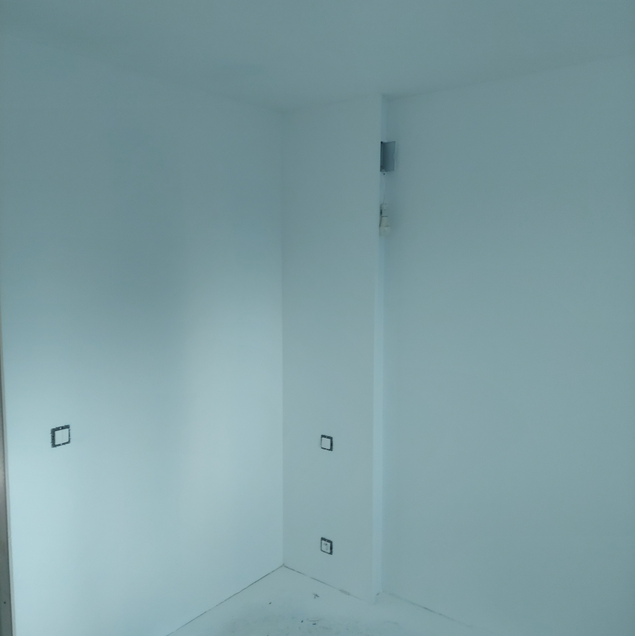 Białe, świeżo pomalowane wnętrze z widocznymi puszkami elektrycznymi, gotowe do montażu gniazdek. Minimalistyczne wykończenie, kąt ujęcia podkreśla przestrzeń.