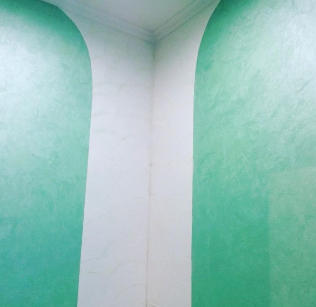 Ściana z dekoracyjną, zieloną farbą w łuki i białą kolumną. Efektowna aranżacja wnętrza z subtelnym wzorem i eleganckim wykończeniem.