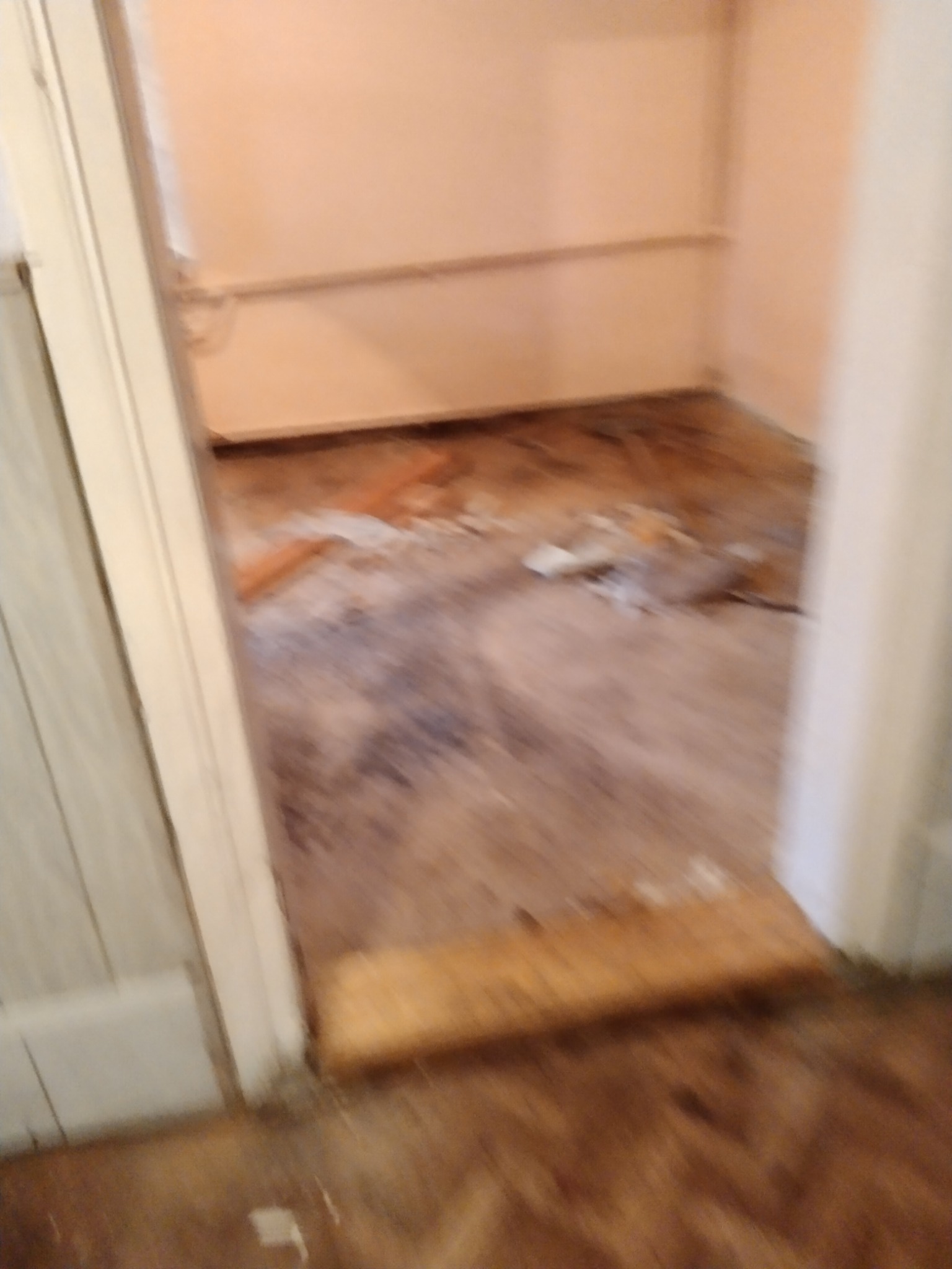 Pokój w trakcie opróżniania; widoczne pozostałości po usuniętych przedmiotach na podłodze i puste ściany w odcieniach beżu.