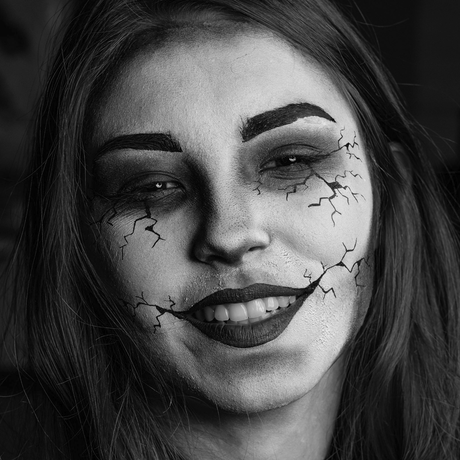 Portret kobiety z artystycznym makijażem imitującym pękniętą porcelanę, czarno-biała fotografia z mocnym kontrastem i ciemną szminką.