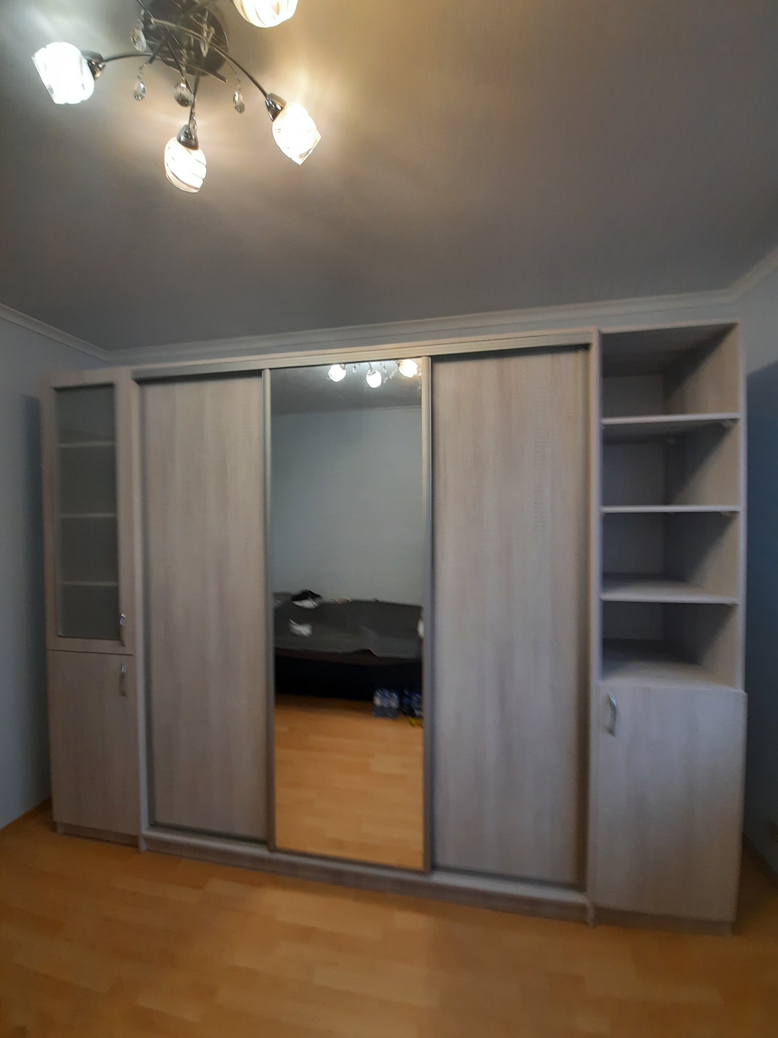 Jasna szafa wnękowa z lustrem i półkami w pokoju. Widoczne przesuwne drzwi i oświetlenie sufitowe. Parkiet na podłodze. Minimalistyczny design.