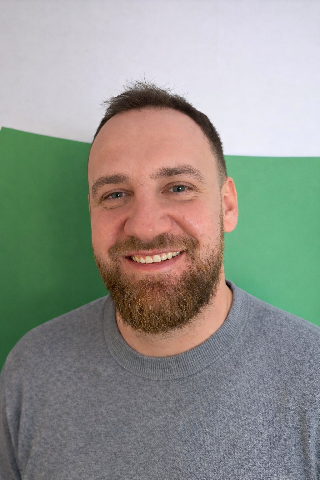 Uśmiechnięty mężczyzna z brodą na tle zielono-białym. Portret w Kczewie, sugerujący profesjonalizm i otwartość.