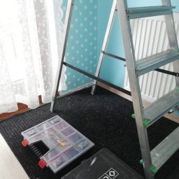 Bartosz Kijas - Rozstawiona aluminiowa drabina w pokoju z turkusową ścianą w białe kropki. Na podłodze skrzynki narzędziowe i dywanik. Widok na okno z białymi zasłonami.