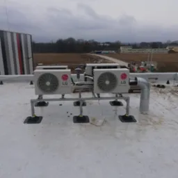 Dwa klimatyzatory LG Dual Inverter na dachu budynku, zamontowane na metalowej konstrukcji. Widoczny system odprowadzania skroplin i elementy mocujące.