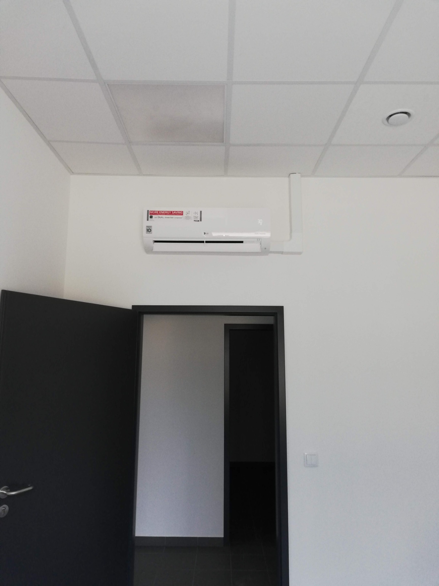 Biała klimatyzacja LG Dual Inverter zamontowana na ścianie w biurze w Tychach. Widoczna sufitowa kratka wentylacyjna i otwarte drzwi.