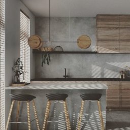 Interior Stories - Minimalistyczna kuchnia z drewnianymi szafkami, betonową ścianą i trzema hokerami pod blatem, oświetlona lampą z drewnianymi akcentami. Żaluzje rzucają cienie na podłogę.