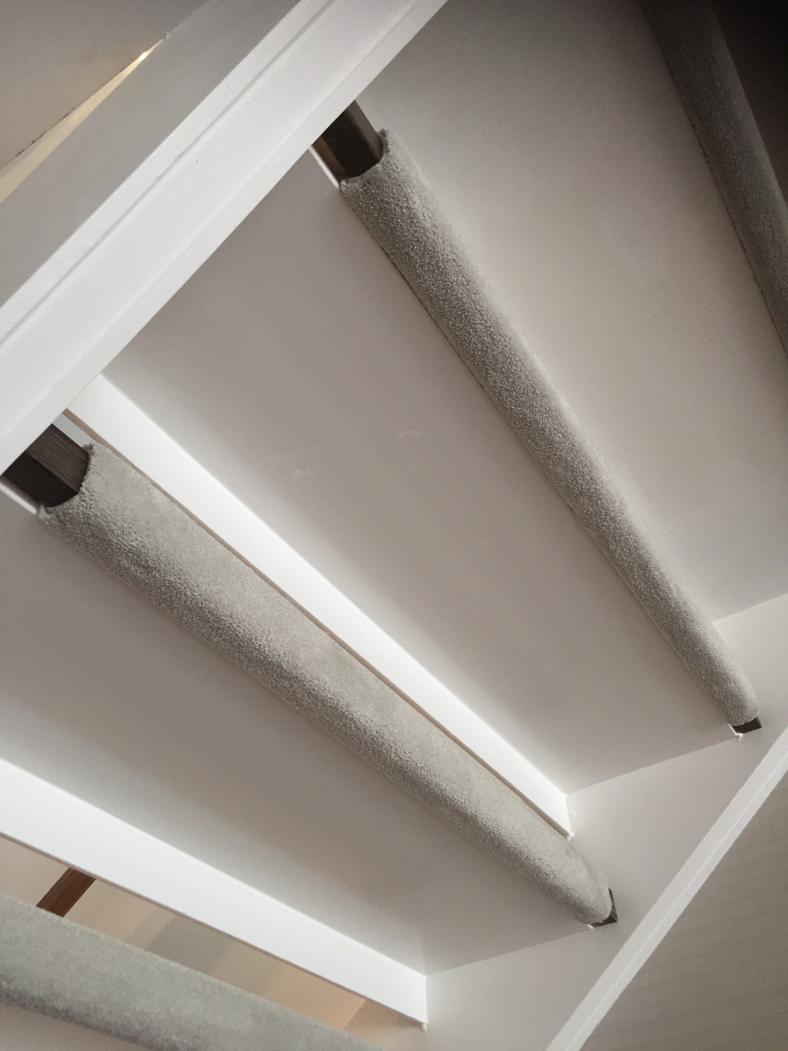 Szczegółowe ujęcie fragmentu schodów z zamontowaną szarą wykładziną na stopniach, widoczne białe elementy konstrukcyjne schodów i fragment ściany.