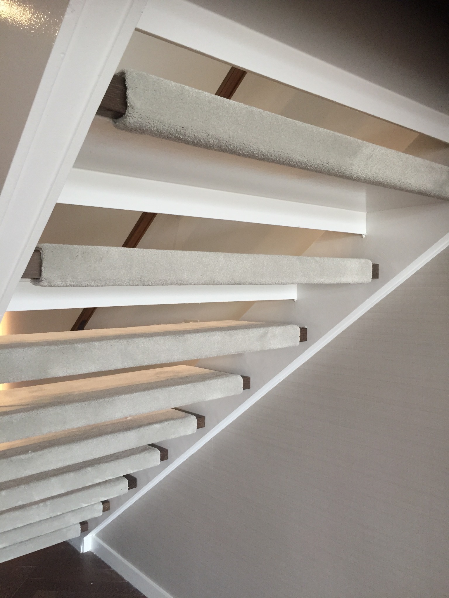 Schody obłożone jasną wykładziną dywanową z widocznymi drewnianymi elementami konstrukcyjnymi i białymi listwami przypodłogowymi.