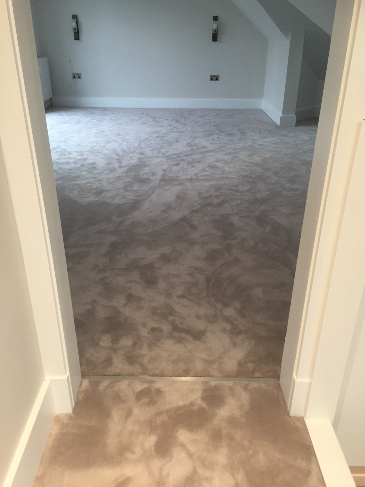 Świeżo położona, beżowo-szara wykładzina dywanowa w jasnym pokoju na poddaszu, widok z progu przez białe futryny drzwiowe.