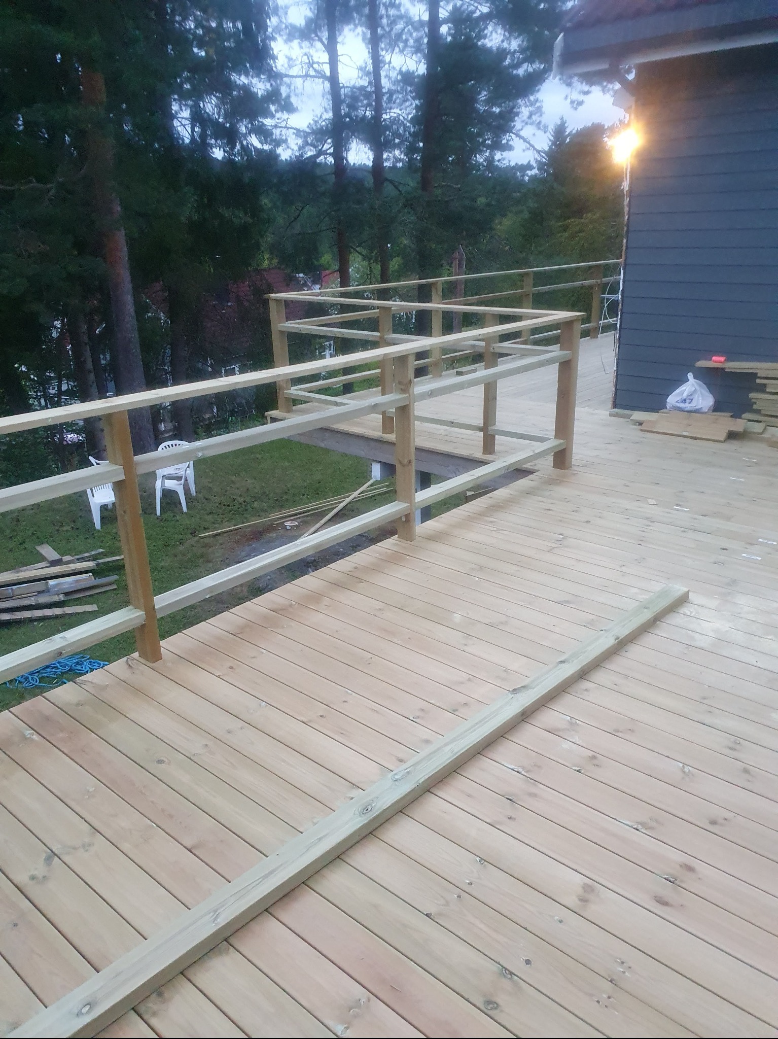 Drewniany taras w trakcie budowy, widoczne deski, balustrady w surowym stanie, narzędzia i materiały budowlane w tle. Budowa tarasu na zewnątrz budynku.